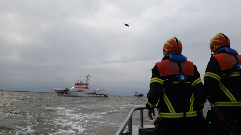 Feuerwehrmänner vor Rettungskreuzer mit Hubschrauber in der Luft